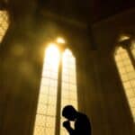person praying in a church with sunny windows